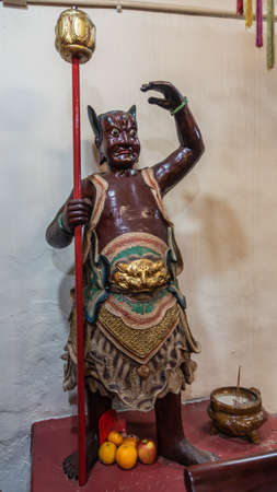 Hong Kong, China - March 7, 2019: Tai O Fishing village. Closeup of fierce-looking brown guardian in God of Sea shrine at Kwan Tai Taoist temple. Gray wall in back.のeditorial素材