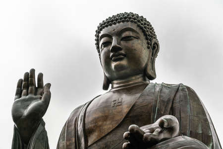 Hong Kong, China - March 7, 2019: Lantau Island. Frontal view of Tian Tan Buddha statue from down under showing face, chest, lotus leaves and stone fence under silver sky.の写真素材