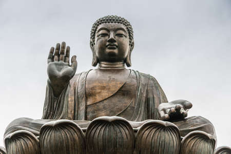 Hong Kong, China - March 7, 2019: Lantau Island. Frontal Facial closeup of Tian Tan Buddha statue from down under showing face, chest, and lotus leaves under silver sky.の写真素材