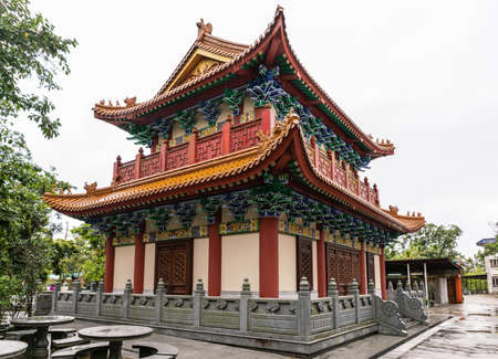Hong Kong, China - March 7, 2019: Lantau Island. Po Lin Buddhist Monastery. Small red-roofed hall under silver sky. Some green foliage. Decorated walls, doors and eaves.のeditorial素材
