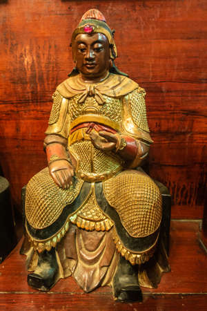 Hong Kong, China - March 8, 2019: Man Mo Yi Tai Taoist Temple in Fu Shin Street. Closeup of idol in gold armor with red wood in back.のeditorial素材