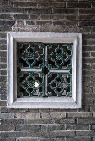 Hong Kong, China - March 8, 2019: Tai Fu Tai Ancestral home in New Territory. Closeup of window and air vent, a square with green decorations set in gray brick wall.のeditorial素材
