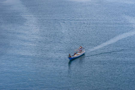 Komodo Island, Indonesia - February 24, 2019: Small white and blue boat on blueish sea water in the bay off Komodo National Park. Steered by young boys trying to sell Komodo Dragon sculptures.のeditorial素材