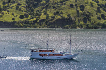 Komodo Island, Indonesia - February 24, 2019: Private white sailing yacht on the move in Komodo Island Bay. Green forested hills in back.のeditorial素材