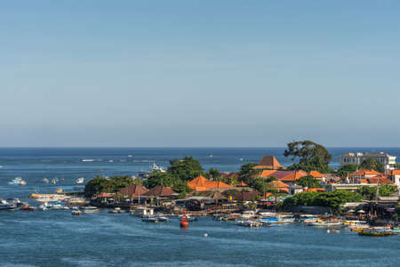 Benoa harbour, Bali, Indonesia - February 26, 2019: The red roofs of the buildings on tip of Tanyung Benoa Peninsula under light blue sky, above dark blue water. Plenty of boats.のeditorial素材