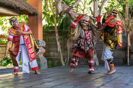 Banjar Gelulung, Bali, Indonesia - February 26, 2019: Mas Village. Play on stage setting. Fleeing Orator in white attacked by man in ugly mask and colorful garments. Other guy tries to stop fight.のeditorial素材
