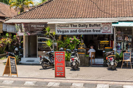 Ubud, Bali, Indonesia - February 26, 2019: Downtown Pedang Tegal, Ji. Hanoman street, commercial district. Front of The Daily Buffer, vegan and gluten free restaurant with motorbikes, flowers and sitting guests.のeditorial素材