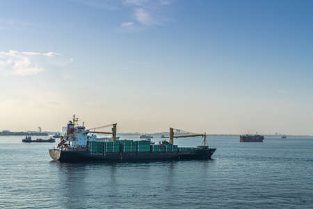 Makassar, Sulawesi, Indonesia - February 28, 2019: Luzon small container ship with its own cranes sails on blue Flores sea off the port of Makassar early morning. Other ships on horizon.のeditorial素材