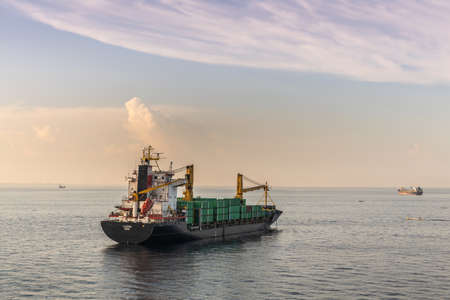 Makassar, Sulawesi, Indonesia - February 28, 2019: Luzon small container ship with its own cranes sails away on blue Flores sea from the port of Makassar early morning. Other ships on horizon.のeditorial素材