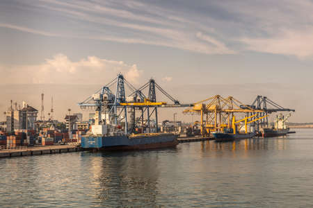 Makassar, Sulawesi, Indonesia - February 28, 2019: Early morning sky over container harbor shows three ships and many cranes with city buildings on horizon.のeditorial素材