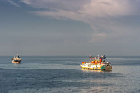 Makassar, Sulawesi, Indonesia - February 28, 2019: Yellow and white Passenger and cargo ship Sabuk Nusantara leaves the harbor on a flat blue sea under a light blue sky.のeditorial素材