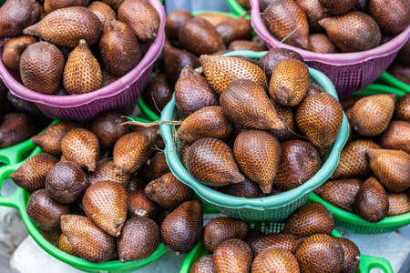 Makassar, Sulawesi, Indonesia - February 28, 2019: Terong Street Market. Closeup of Green and purple baskets filled with brown snake fruits.の写真素材