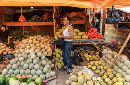 Makassar, Sulawesi, Indonesia - February 28, 2019: Terong Street Market. Fruit booth offers heaps of different kinds, ball size large and small under yellow tarp with two male vendors.のeditorial素材