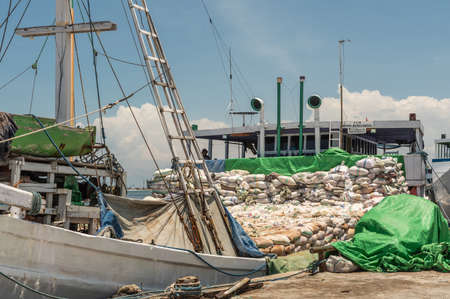 Makassar, Sulawesi, Indonesia - February 28, 2019: Paotere Old Port. White Amran Berkembang island transport boat almost fully loaded with bags sits at dock under blue sky.のeditorial素材