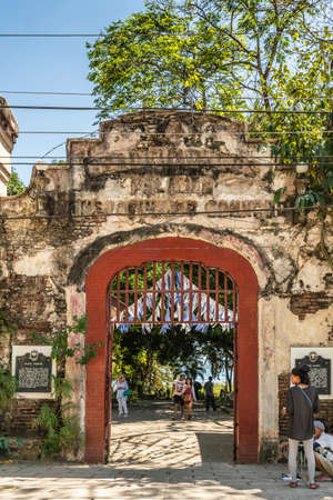 Puerto Princesa, Palawan, Philippines - March 3, 2019: Historic stone gate to Plaza Quartel shows red door frame, brown stones , people, blue sky and green foliage.のeditorial素材