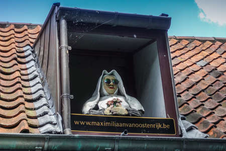 Bruges, Flanders, Belgium -  June 17, 2019: Closeup of nun with sun glasses sculpture set in roof window of restaurant Maximiliaan van Oostenrijk. Red roof, blue sky.のeditorial素材