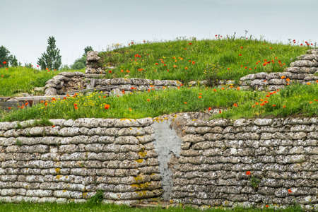 Diksmuide, Flanders, Belgium -  June 19, 2019: Historic WW1 Trenches, called Dodengang along IJzer River, shows gray-brown stone-hard sandbags, green grass, red poppies and blue sky.のeditorial素材