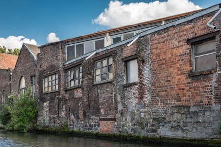 Gent, Flanders, Belgium -  June 21, 2019: Old red-brown brick industrial warehouses along the Lieve River under blue sky with white cloud patches. Greenish water.の写真素材