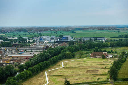 Diksmuide, Flanders, Belgium -  June 19, 2019: View on farms and farm land and industrial area with Deceuninck plant from up IJzertoren, tallest peace monument of WW 1. Greens, grays and reds.のeditorial素材