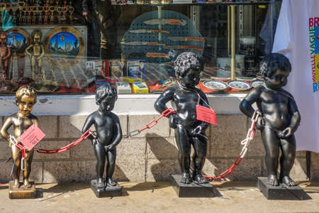 Brussels, Belgium - June 22, 2019: Closeup of chained group of metalic Manneken Pis statues in front of gift store and its display window.のeditorial素材