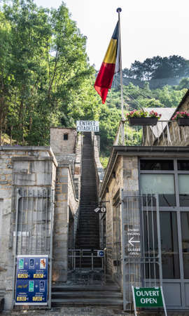 Dinant, Belgium - June 26, 2019: Entrance to the long naroow brown stone stairway up to the citadel, captured in green foliage and Belgian flag in front.のeditorial素材