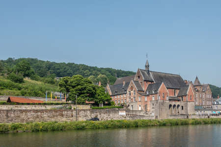 Dinant, Belgium - June 26, 2019: Part of Red stone ancient convent of the Capuchins is now the seat of CPAS, the social services of the city. Meuse River in front, blue sky.のeditorial素材