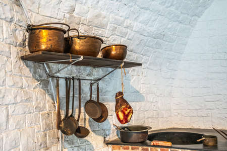 Dinant, Belgium - June 26, 2019: Inside Citadelle. Part of historic army kitchen with copper pots, ham and stove against white painted wall.のeditorial素材