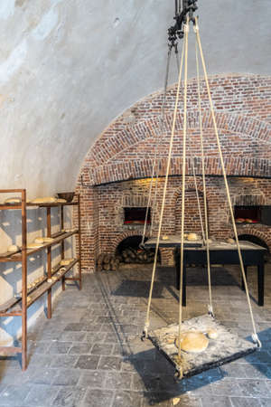 Dinant, Belgium - June 26, 2019: Inside Citadelle. Part of historic bakery with shelves of bread, several open brick stone ovens, and a giant balance to weigh dough. White walls and ceililng.のeditorial素材