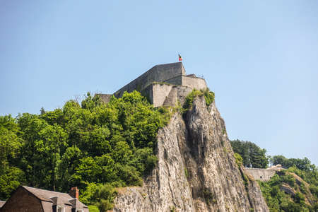 Dinant, Belgium - June 26, 2019: Closeup of fish eye view of Citadelle front top with Belgian flag under blue sky and green foliage.の写真素材