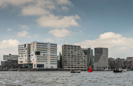 Amsterdam, the Netherlands - June 30, 2019: Cubic modern architecture of white large Justice Palace on IJdok under blue sky with white clouds. Other office buildings. Pedestrian bridge and IJ water.のeditorial素材