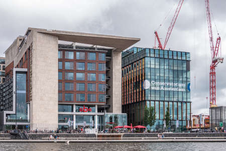 Amsterdam, the Netherlands - July 1, 2019: Library and Conservatorium modern buildings of the city under heavy cloudscape and with red construction cranes on the side.のeditorial素材
