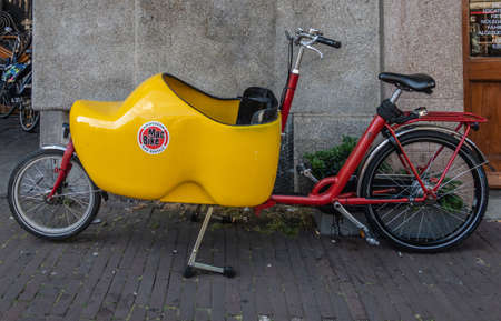 Amsterdam, the Netherlands - July 1, 2019: Closeup of parked bakfiets, front-trunk bike to transport a load or a child. Trunk in shape of yellow clog.のeditorial素材