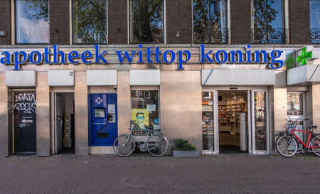 Amsterdam, the Netherlands - July 1, 2019: Facade of pharmacy Wittop Koning with bikes in front, dark blue name sign and the classic green cross light. Located in street called Overtoom.のeditorial素材