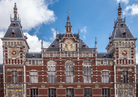 Amsterdam, the Netherlands - July 1, 2019: Red brick with white trim upper part facade Centraal Railway Station with towers, clocks, and plenty of frescoes under blue sky with white clouds.のeditorial素材