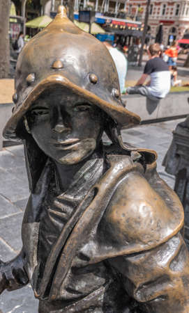 Amsterdam, the Netherlands - July 1, 2019: De Nachtwacht compostion of statues on Rembrandtplein. closeup of chest and head of Boy with helmet statue against people and buildings.のeditorial素材