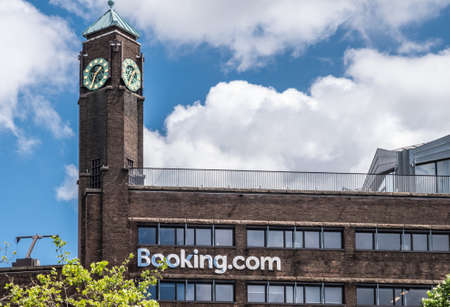 Amsterdam, the Netherlands - July 1, 2019: Rembrandtplein. De dark brown brick office building with clock tower of booking.com against blue sky and white clouds.のeditorial素材