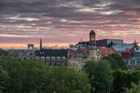 Amsterdam, the Netherlands - July 2, 2019: Yellow and red lights cut by dark clouds in sky over towers and roofs. Leidseplein up front. Westerkerk spire. Modern Pontsteiger high rise.のeditorial素材