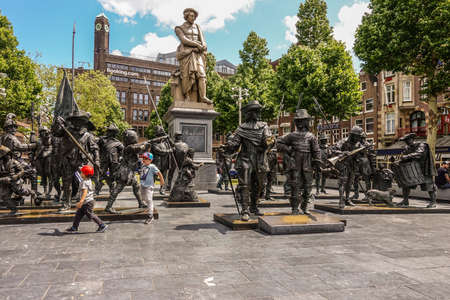 Amsterdam, the Netherlands - July 1, 2019: De Nachtwacht compostion of statues on Rembrandtplein in front of beige tall statue of Rembrandt Van Rijn, with booking.com office buildign in back.のeditorial素材