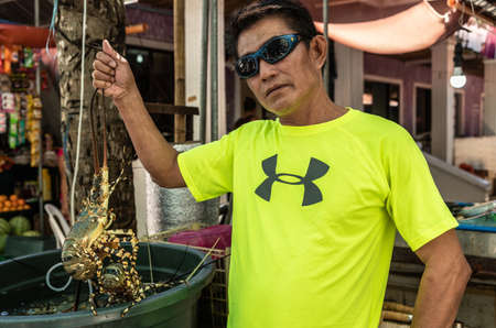 Balabag, Boracay Island, Philippines - March 4, 2019: Endeqal Seafood along alley off White Beach. Vendor with bright lemon-yellow shirt and sunglasses shows live lobster, out of large vat.のeditorial素材