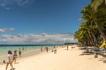 Balabag, Boracay Island, Philippines - March 4, 2019: White beach shows sand and azure sea with wall of palm trees. People in water. Cloudscape in blue sky.のeditorial素材