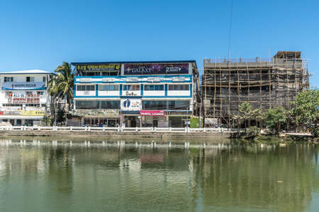 Balabag, Boracay Island, Philippines - March 4, 2019: Multiple businesses in four story buildings under blue sky on other side of greenish Balabag lake. One building under construction.のeditorial素材