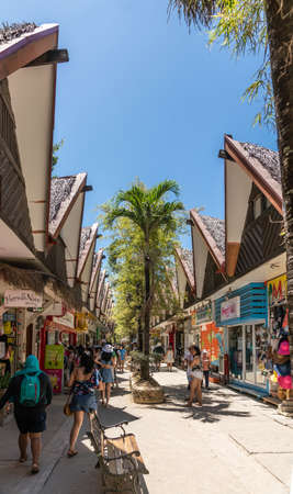 Balabag, Boracay Island, Philippines - March 4, 2019: DâMall de Boracay. Line of small stores with brown and straw roofs and shoppers in the alley under blue sky with green palm trees.のeditorial素材