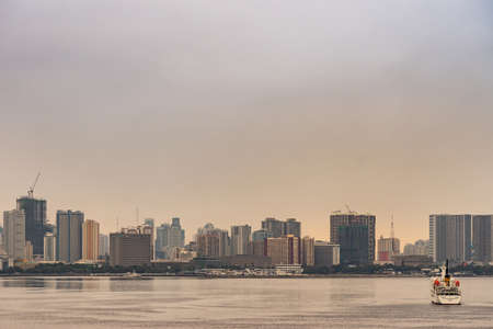 Manila, Philippines - March 5, 2019: South Harbor area early morning. Skyline with tall buildings, some under construction with Amosud rescue ship on sea. Silver sky.のeditorial素材