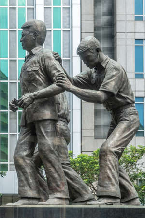 Manila, Philippines - March 5, 2019: Bronze Benigno Aquino, Jr. monument on Ayala triangle for the assassinated politician in financial district with wall of skycraper at background. Some green fioliage.のeditorial素材