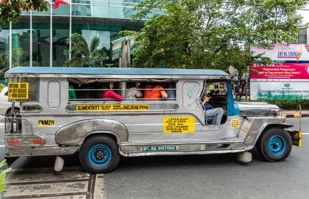 Manila, Philippines - March 5, 2019: Metalic long Jeep Public Transport in street. Side view. Full of people. Green foliage.のeditorial素材