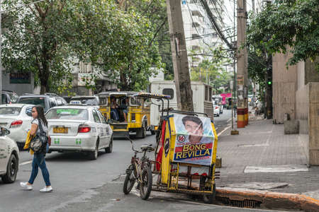 Manila, Philippines - March 5, 2019: Red-yellow Tricycle taxi with large poster of Bong Revilla, actor and politician in street with cars, gray buildings and green foliage.のeditorial素材