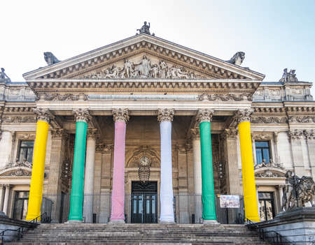 Brussels, Belgium -  June 22, 2019: Brown stone Front facade with tall columns and tympanum with statues on top. Pillars wrapped in bright colors of the Stock Exchange building, Bourse de Bruxelles . Silver sky.のeditorial素材