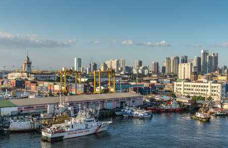 Manila, Philippines - March 5, 2019: South Harbor evening twilight. Philipine Coast Guard vessel and busy harbor activities, with tall office buildings on horizon under light blue sky.のeditorial素材