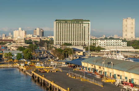 Manila, Philippines - March 5, 2019: South Harbor evening twilight. iconic and historic The Manila Hotel a block away. Port acitivity in front, high rise buildings on horizon under blue sky.のeditorial素材