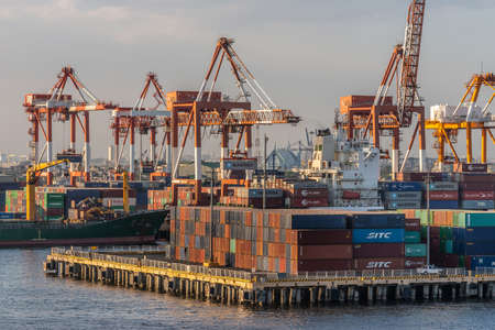 Manila, Philippines - March 5, 2019: South Harbor evening twilight. Closeup of combination of shipping containers, multiple cranes, and ships under cloudscape.のeditorial素材